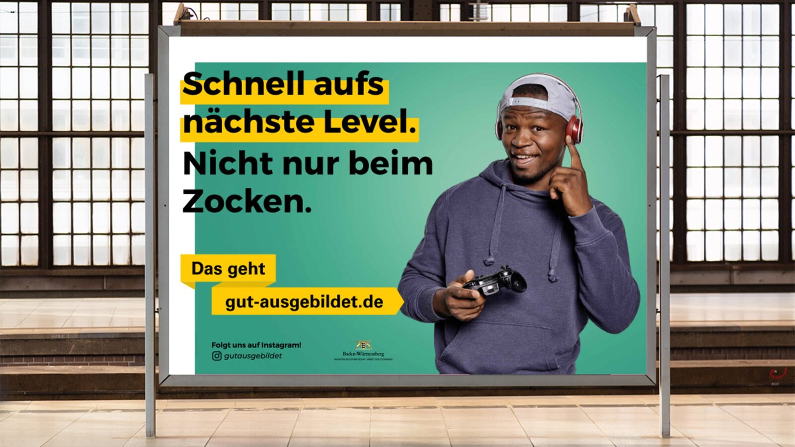 Plakat zeigt „gut ausgebildet” Werbung mit dem Schriftzug: „Schnell aufs nächste Level. Nicht nur beim Zocken.” Daneben ist ein Mann mit Kopfhörern und einem Controller.